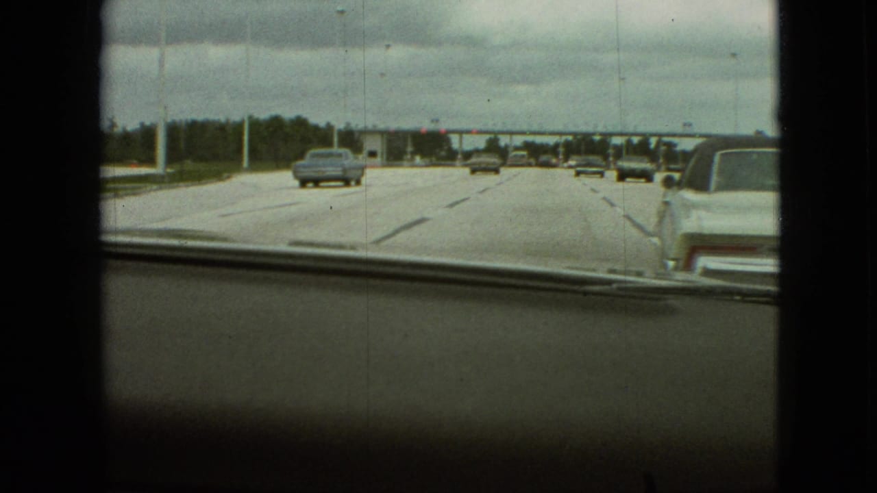 Highway lanes seen through a windshield with cars traveling toward a toll plaza.