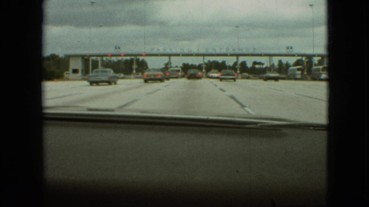 Several cars continue toward a parking entrance structure seen through a windshield.