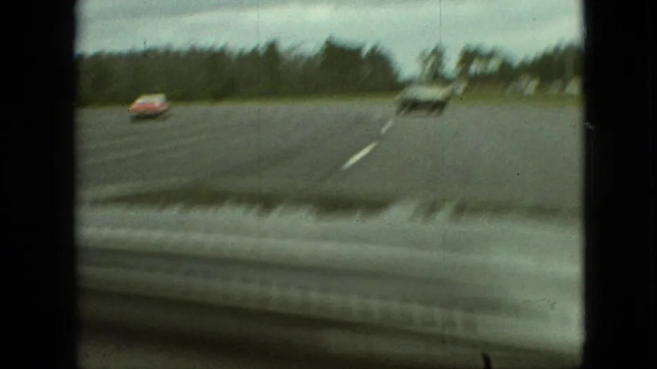 A forward-facing home-movie view shows several period cars on a broad road in the Branson area, with trees beyond the pavement.