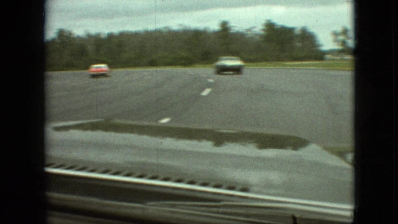 1968 Branson, Missouri home-movie frame from inside a moving car, showing a wet curving road, overcast sky, trees, and two distant oncoming vehicles.