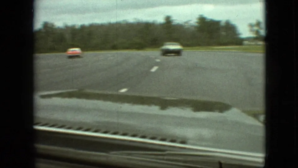 1968 Branson, Missouri home-movie frame from inside a moving car, showing a wet curving road, overcast sky, trees, and two distant oncoming vehicles.