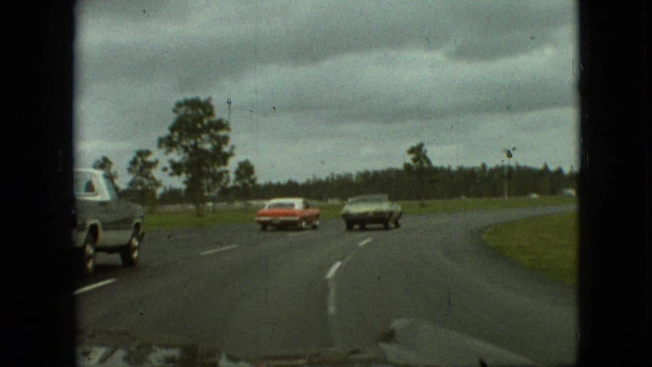 1968 Branson, Missouri home-movie frame showing a red sedan and dark coupe ahead on a curving two-lane highway, with a partial vehicle at the left edge and trees beyond the road.