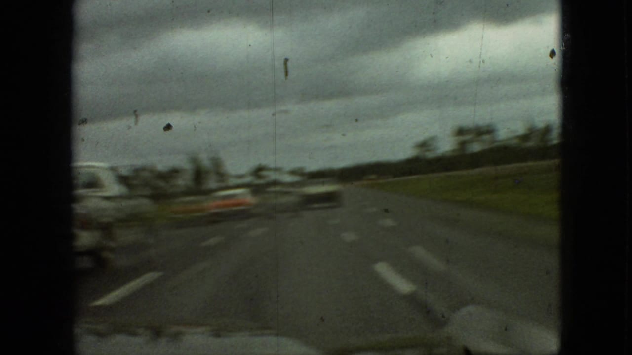 Moving highway view with blurred cars, grassy roadside, and heavy clouds.
