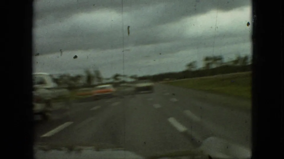 1968 Branson, Missouri home-movie frame showing a moving car perspective on a highway with blurred vehicles and an open grassy shoulder.