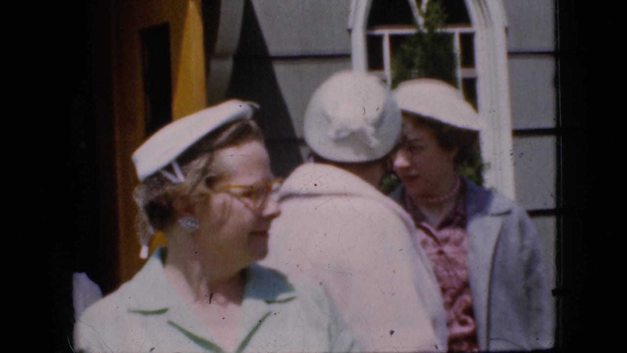 California 1969 8mm frame of women in pastel clothing and white hats outside a church entrance with a yellow door and arched window.