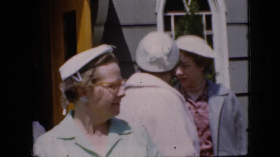 California 1969 8mm frame of women in pastel clothing and white hats outside a church entrance with a yellow door and arched window.
