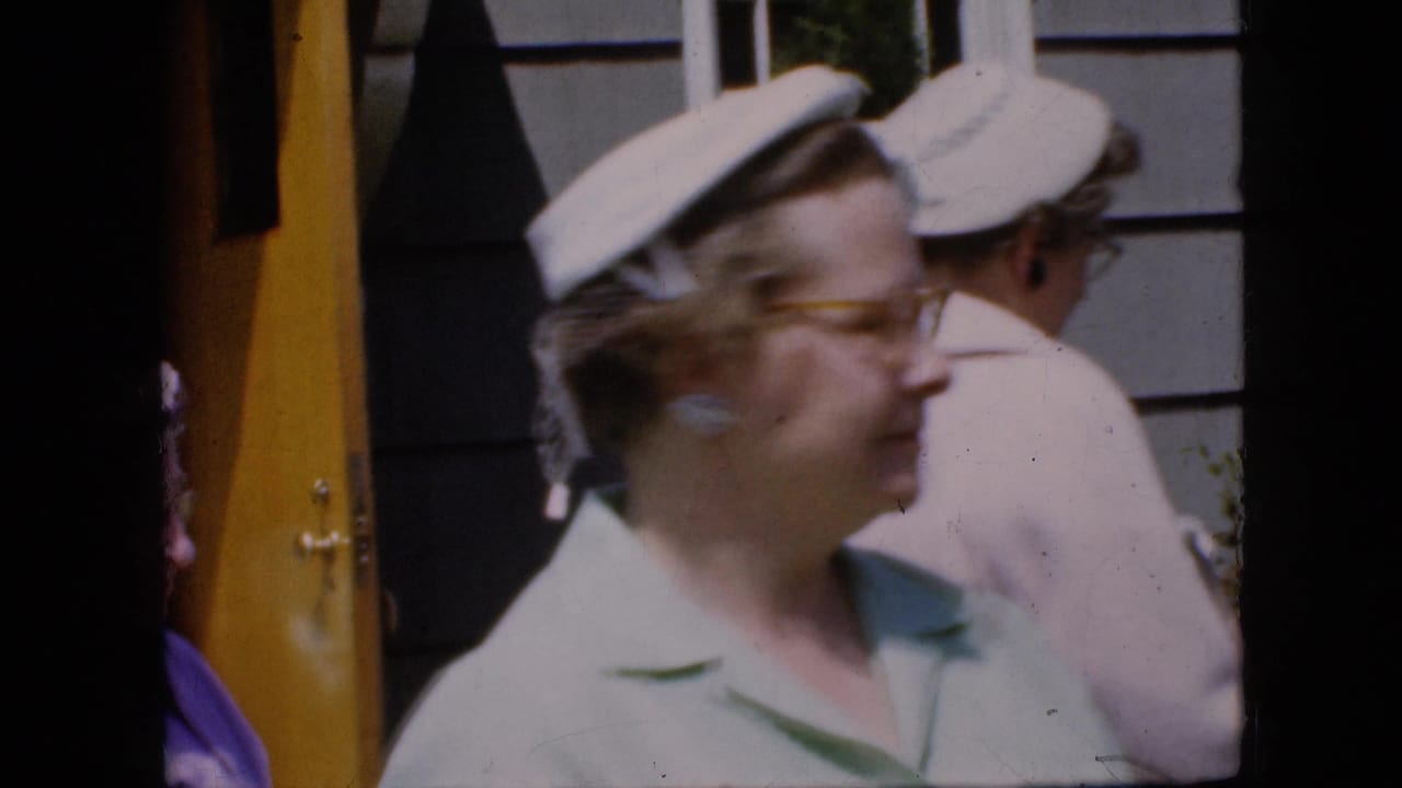 A woman in glasses and a white hat passes in front of a yellow doorway.