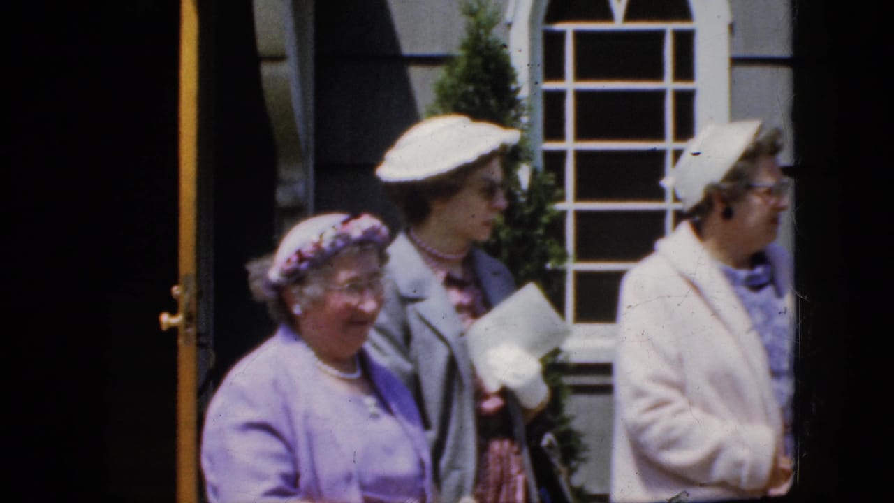 Several adult women in hats stand beside a window and dark doorway.