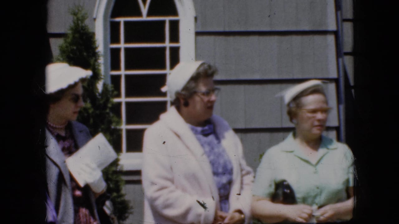 Three older women in 1969 California home-movie footage stand outside a gray shingled house, with one holding papers and two wearing light-colored hats.