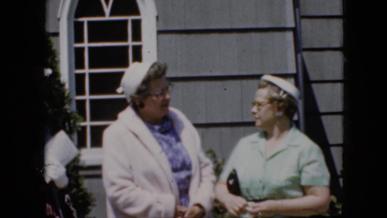 Two older women in supplied 1969 California footage face each other near a white arched window, with a third woman partly visible at the edge.