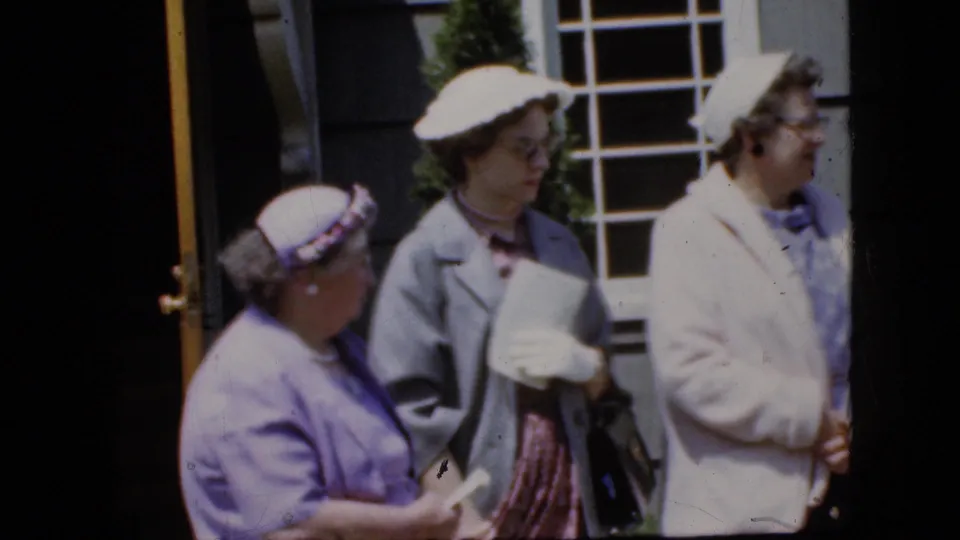 Three adult women wearing hats, light coats, gloves, and pastel clothing stand outside a California house in the supplied 1969 home-movie footage.