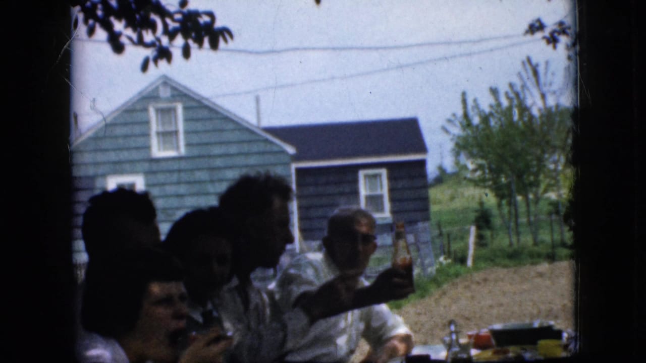 Family members seated at an outdoor table with food and bottles, with a blue house behind them.