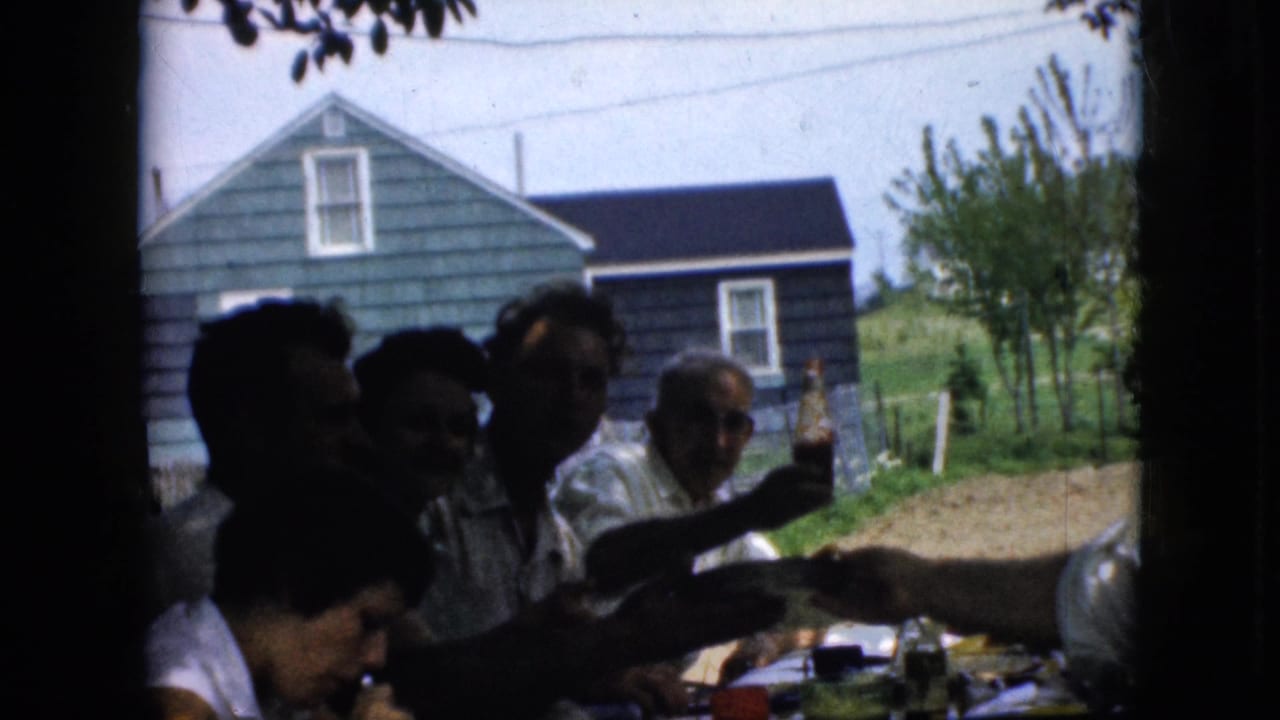 People seated around a shaded outdoor table while a man holds up a bottle.