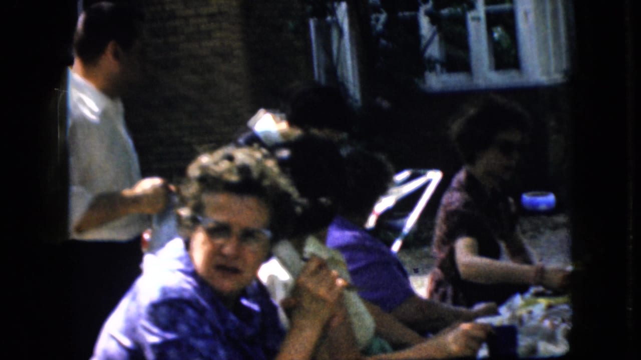 Women seated at an outdoor table while a man in a white shirt stands nearby.