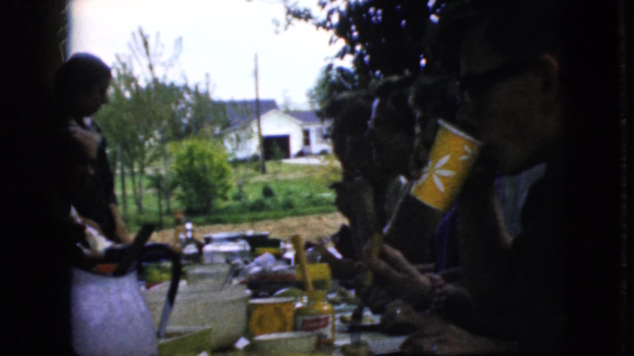 A person holds a yellow patterned cup beside a crowded outdoor lunch table.