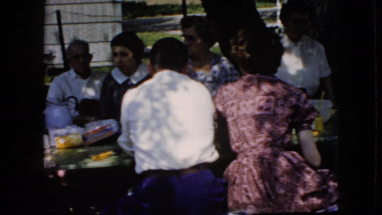 Adults gathered around an outdoor picnic table in dappled shade.