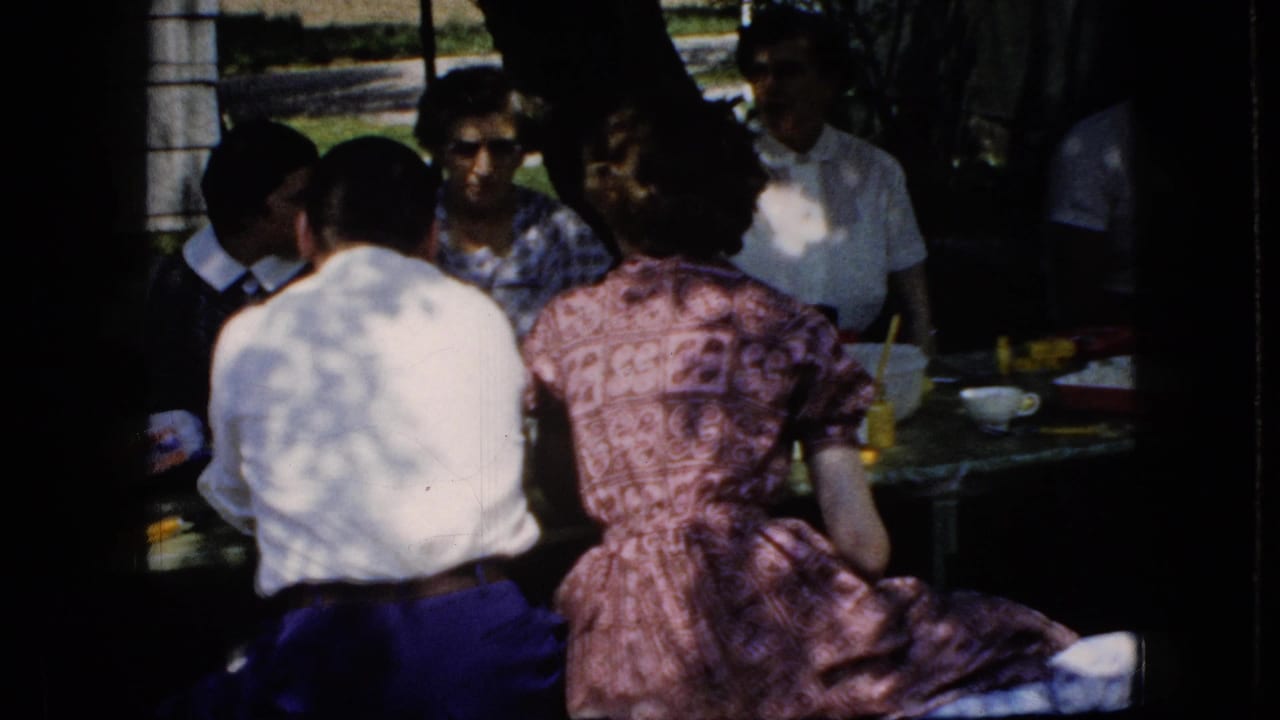 Group of adults seated at a picnic table beneath trees.
