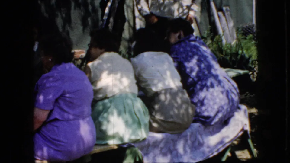 California 1969 home-movie frame showing a closer view of adult women seated on benches at a church picnic in dappled shade.