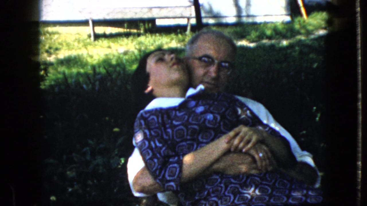 Woman leans back against an elderly man as he holds her on the grass.
