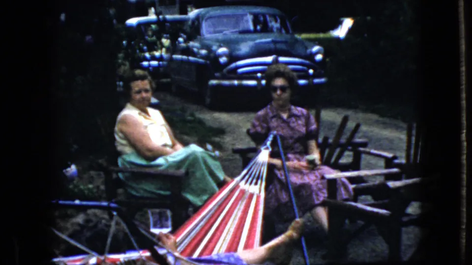 The final frame shows the same 1969 California backyard moment, with two women seated beside a red, white, and blue hammock, another person's legs in the foreground, and an older dark sedan parked among trees behind them.