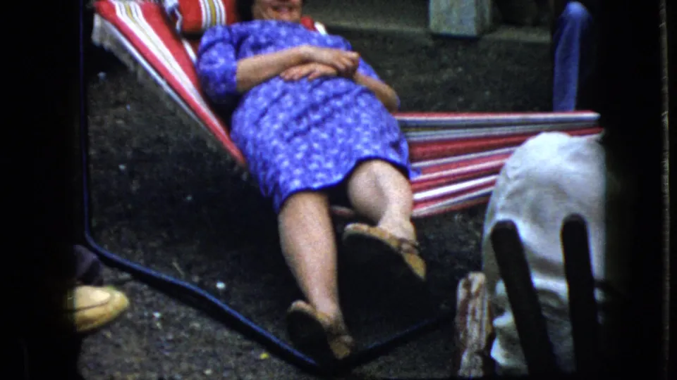 The 1969 California frame shows the woman lying back in the striped hammock, smiling faintly, with another person's legs partly visible near the lower right edge.