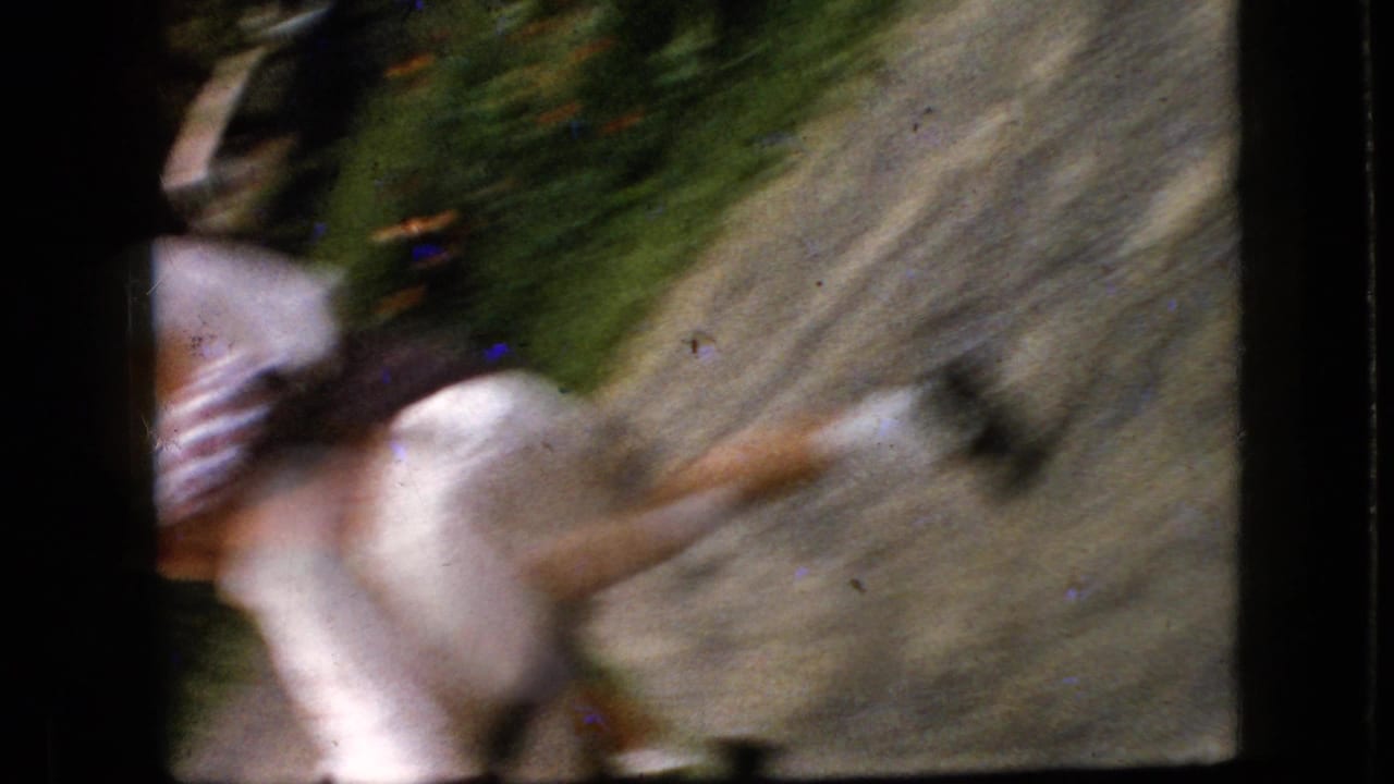 A blurred woman moves across a gravel or dirt path beside greenery.