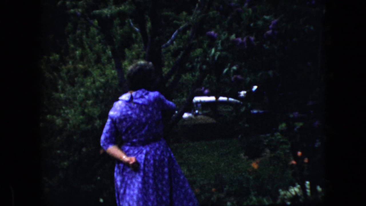 Woman in a purple patterned dress walking through a shaded garden.
