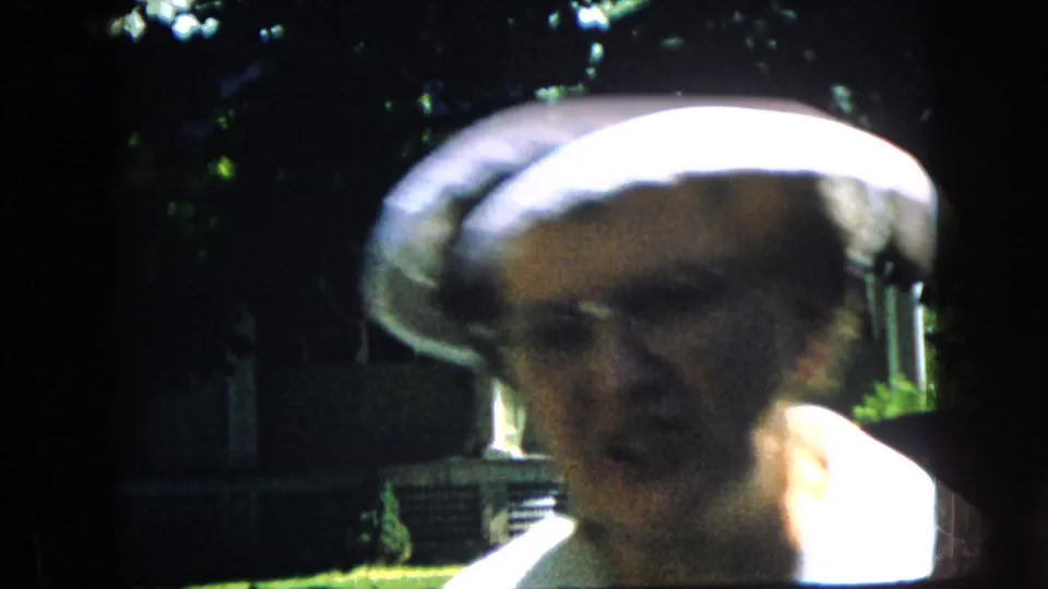 In this California 1969 8mm frame, an older woman wearing a white hat appears very close to the camera, with her face partly soft from motion and strong sunlight.
