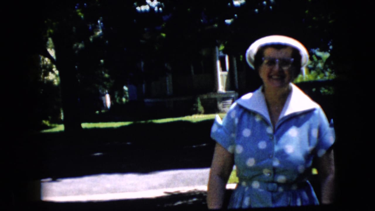 Older woman smiling closer to the camera with trees and a street behind her.