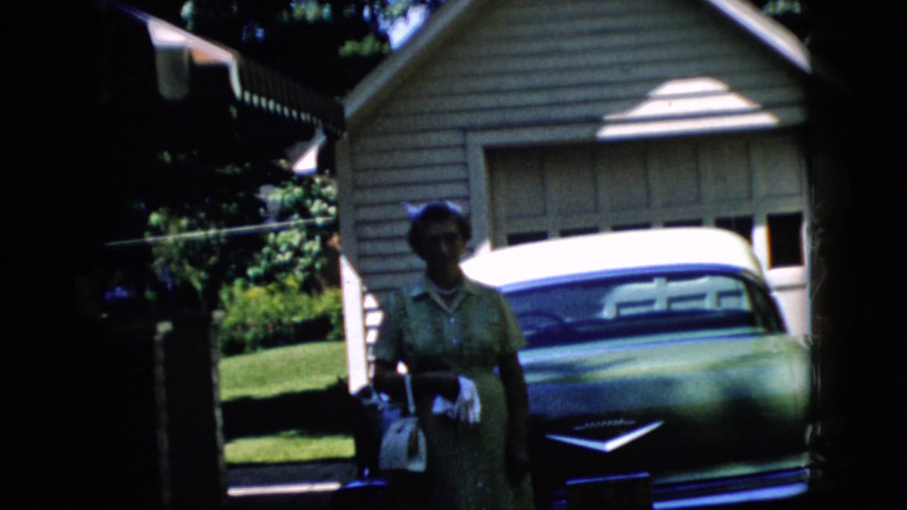 Woman standing near a classic car in a driveway in front of a garage.