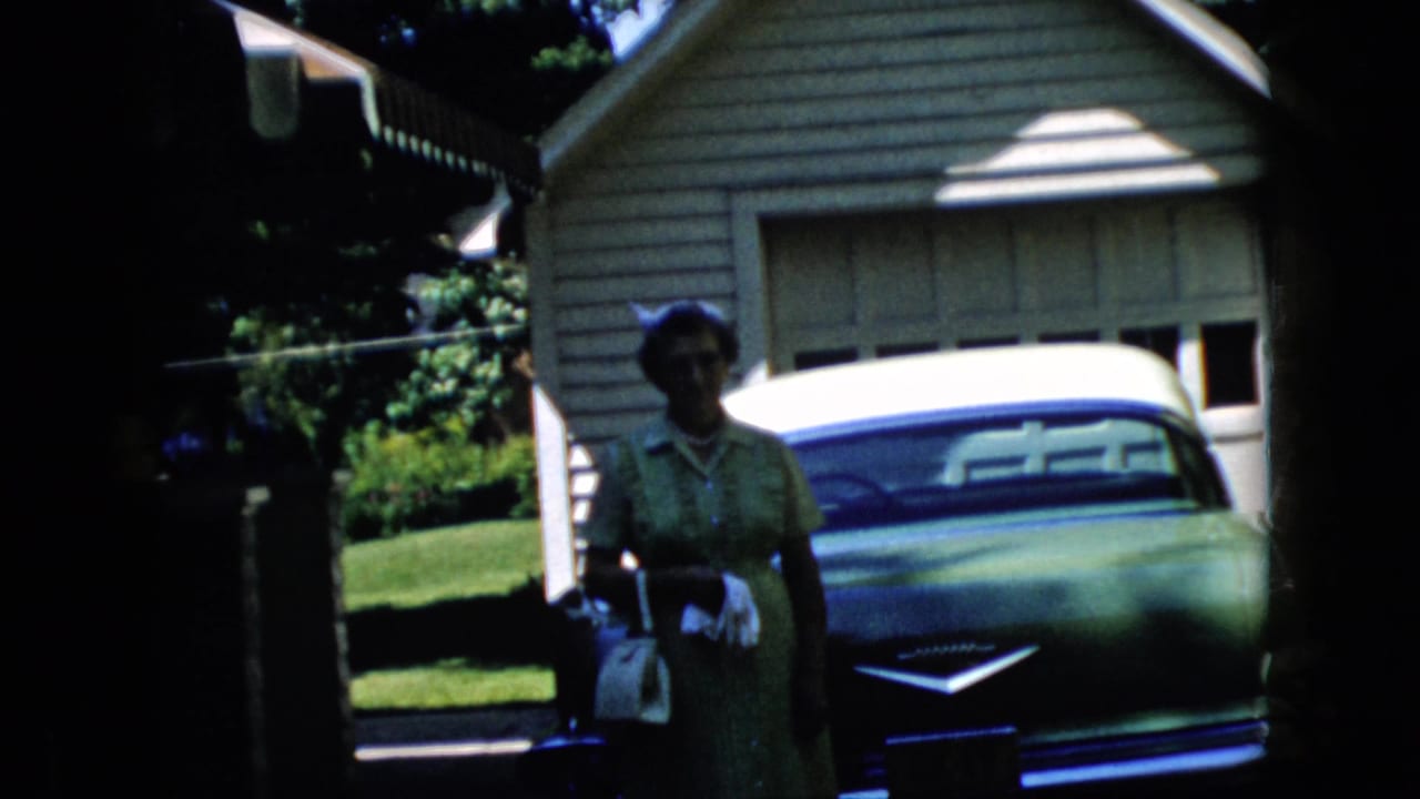 Woman beside a car with a garage and house exterior behind her.