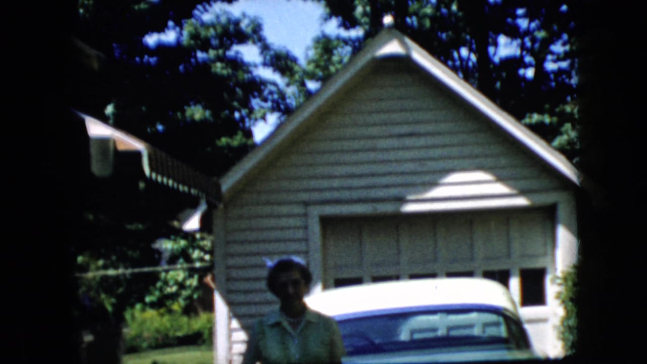 Woman is partly lower in frame near a green car in front of a garage.