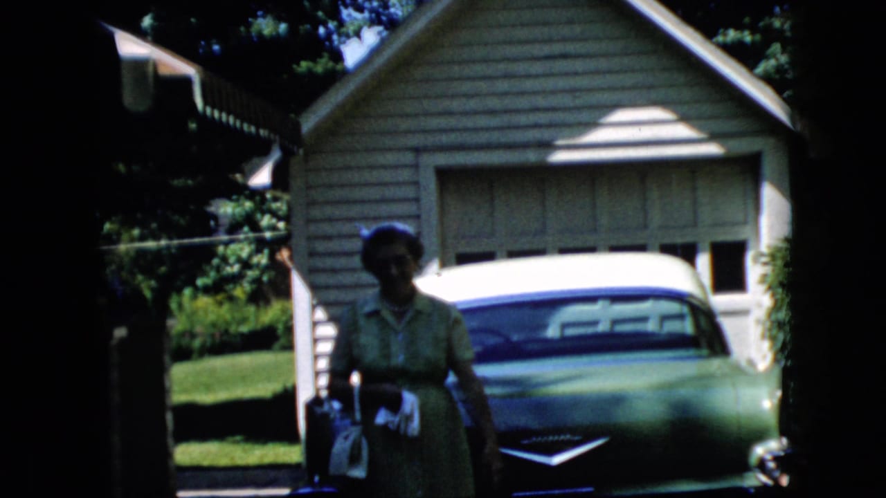 Woman standing beside a green-and-white car in front of a detached garage.