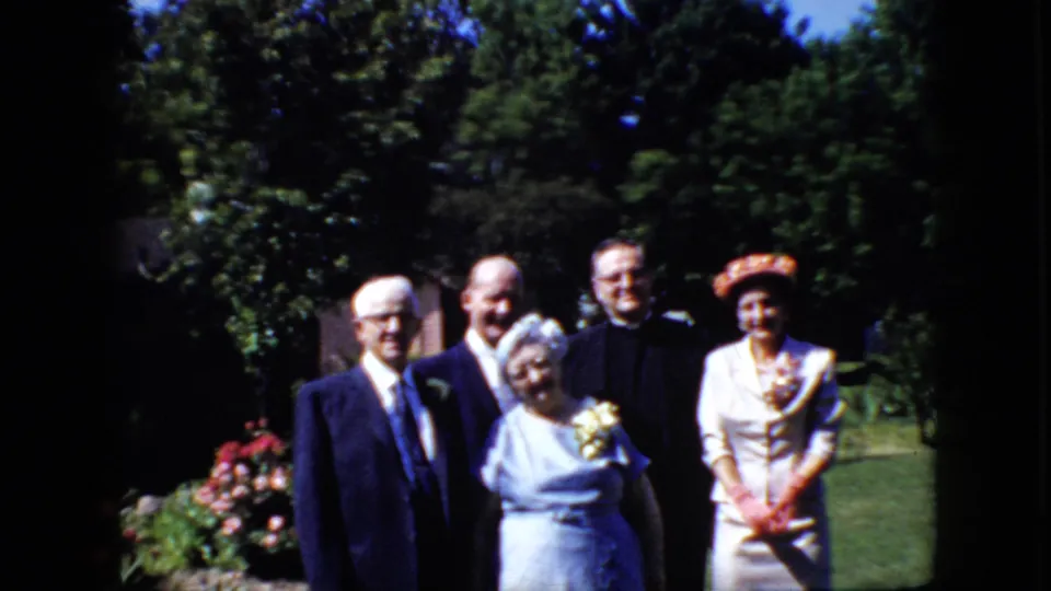Five adults pose in the sunny California yard, including the senior couple, two men in dark formal clothing, and a woman in a white dress and hat.