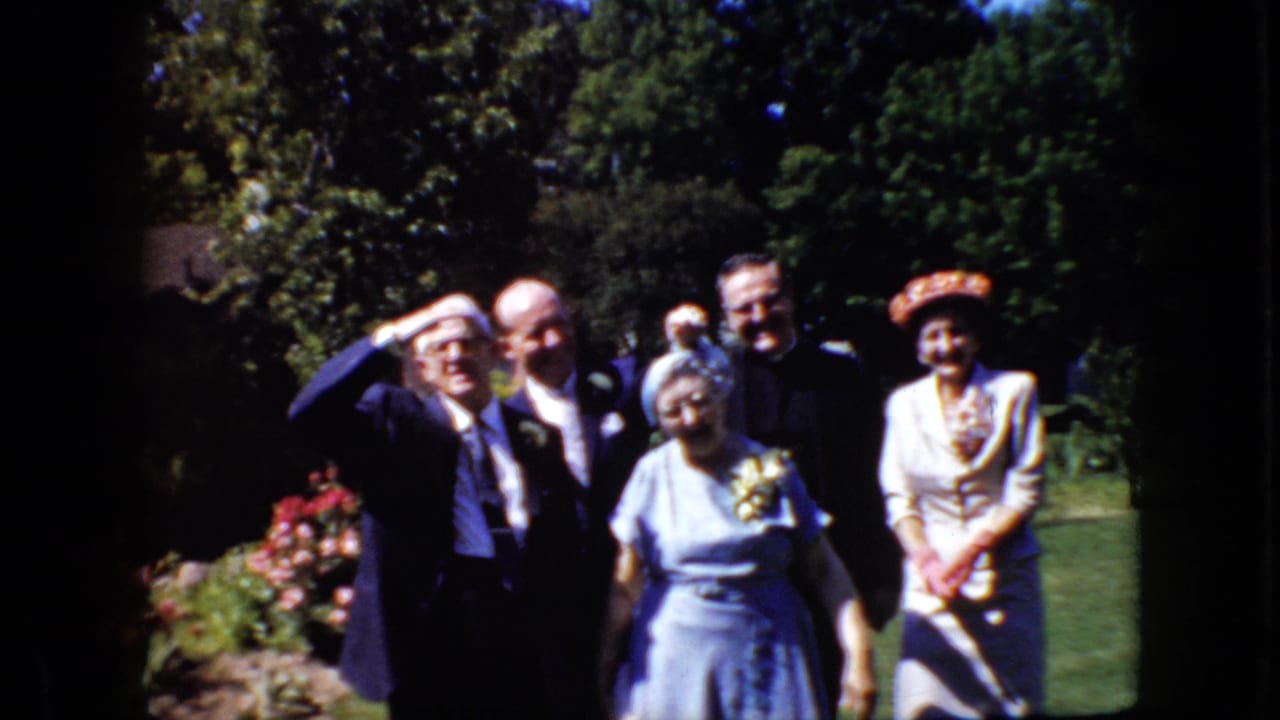 In this 1969 California home-movie frame, formally dressed adults stand in a garden with men in suits and women in dresses and hats facing the camera.