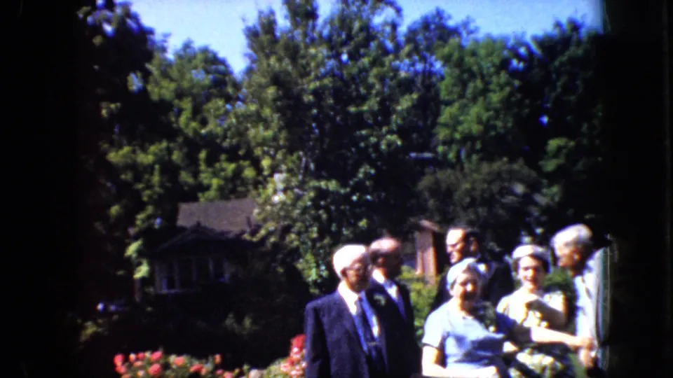 Older adults in formal summer clothing gather in a landscaped California garden at the end of the supplied 1969 8mm clip.