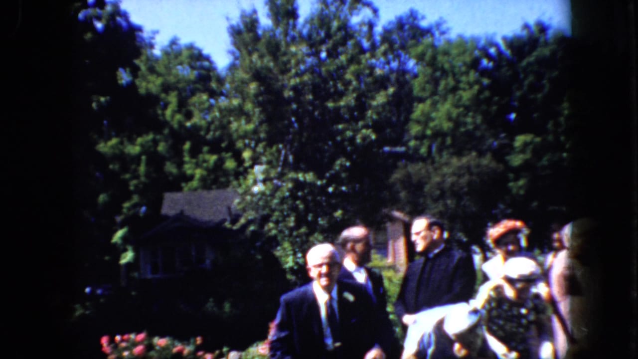 Wedding guests throw rice toward the older couple in an outdoor garden setting.