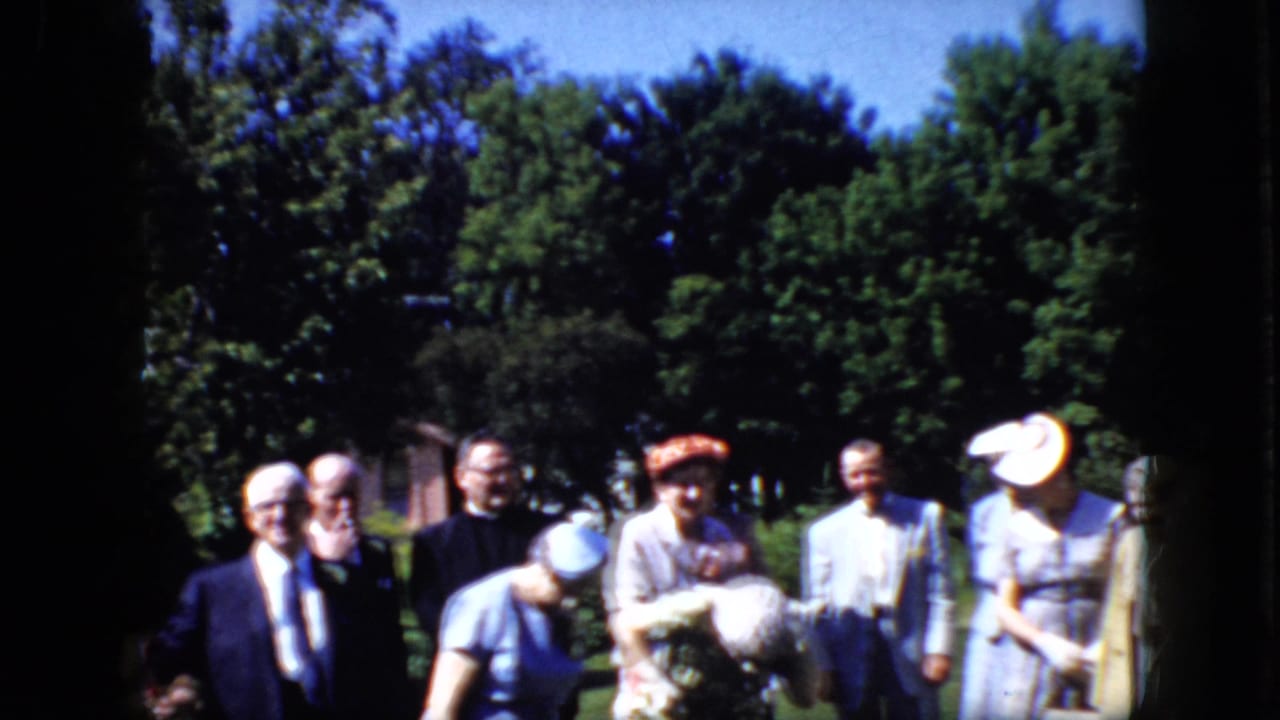A group of adults laugh and bend forward outdoors beside trees.