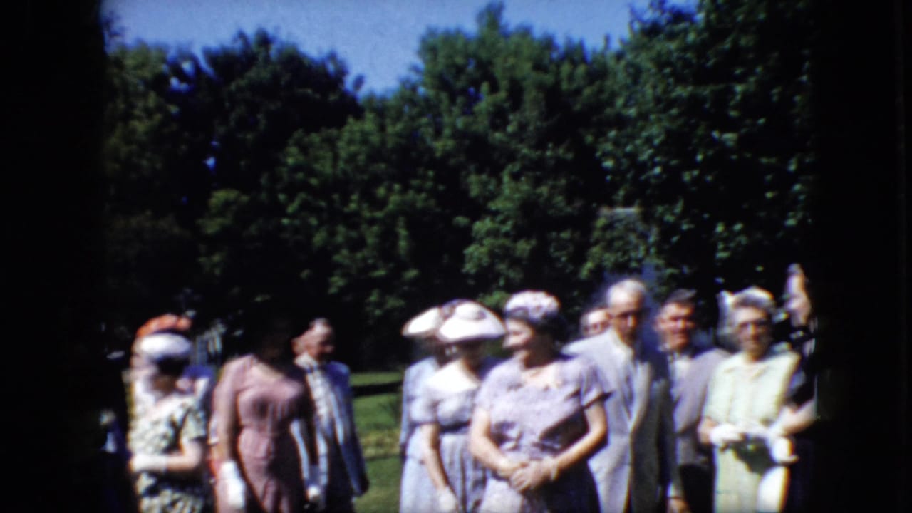 A group of older adults stands outdoors, with several people facing the camera and others turned in conversation.