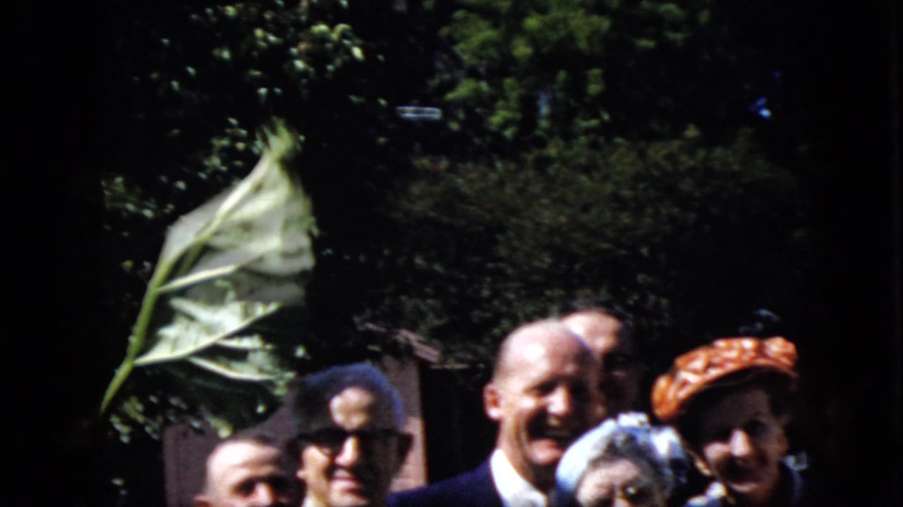 Adults smiling toward the camera outdoors with a large leaf crossing the left side of the frame.