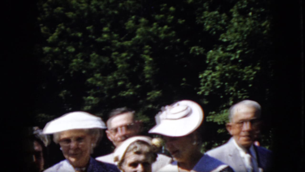 A group of older adults, several wearing prominent white hats, stands close together outdoors against dense green foliage in California footage from 1969.