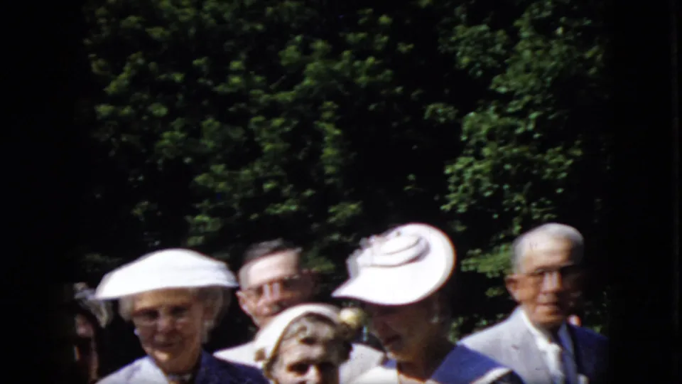 A group of older adults, several wearing prominent white hats, stands close together outdoors against dense green foliage in California footage from 1969.