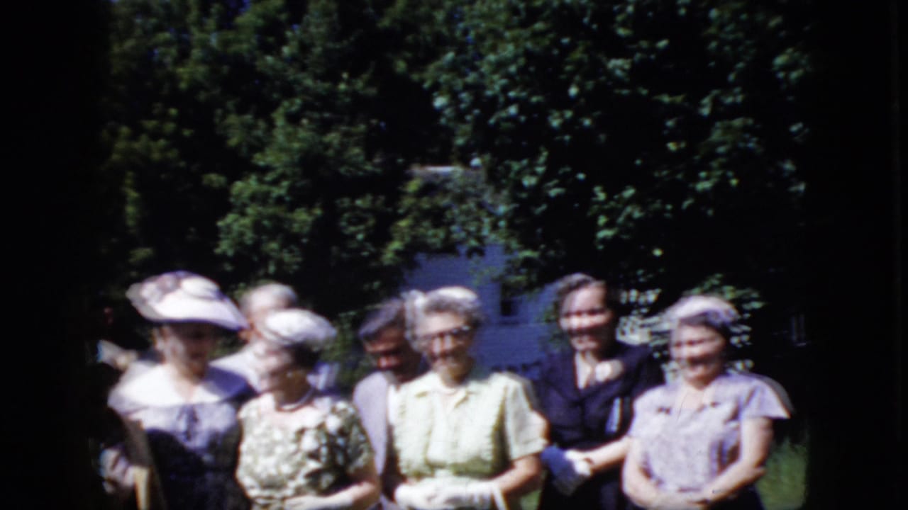 Older adults standing together outdoors in a garden with trees behind them.