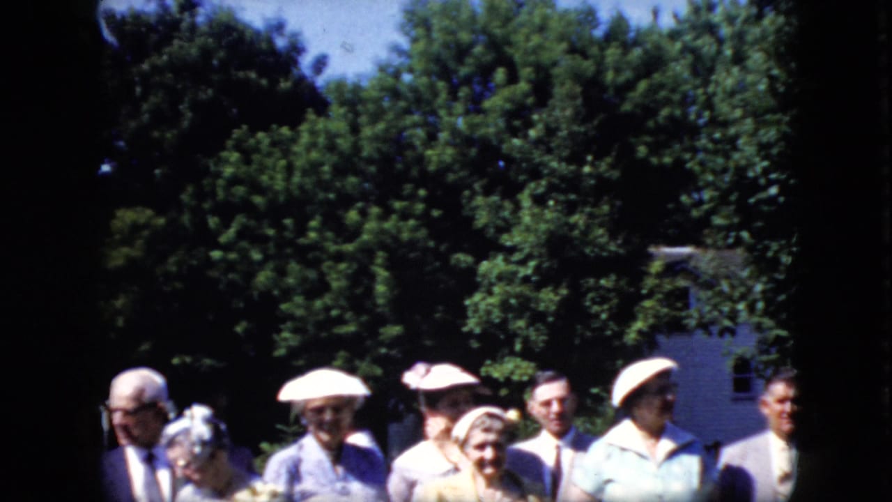 Part of the adult group standing outdoors, including women in hats and a man in a suit near trees.