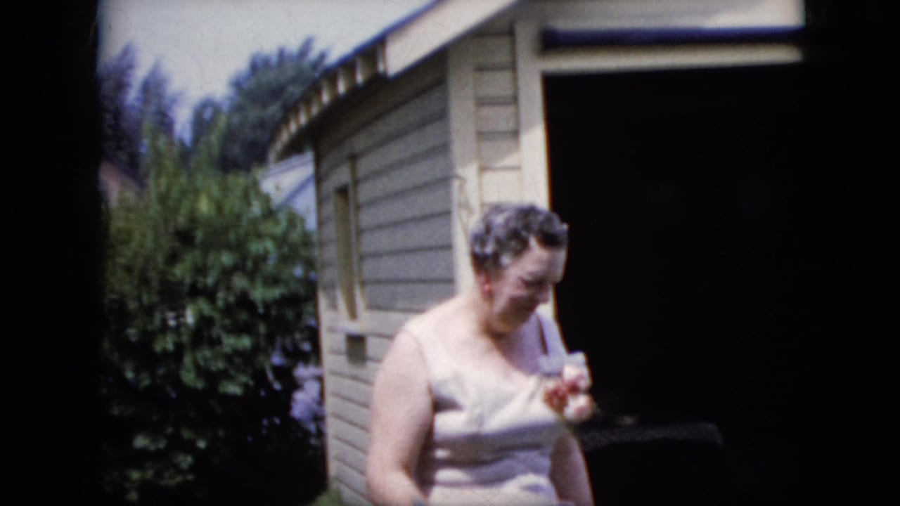 Woman looks downward while holding a small object near a dark doorway.
