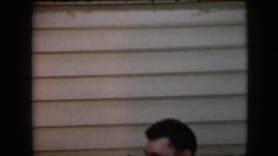 A partial dark-haired head appears at the lower edge of the frame beneath beige horizontal siding, with the rest of the residential exterior mostly empty.