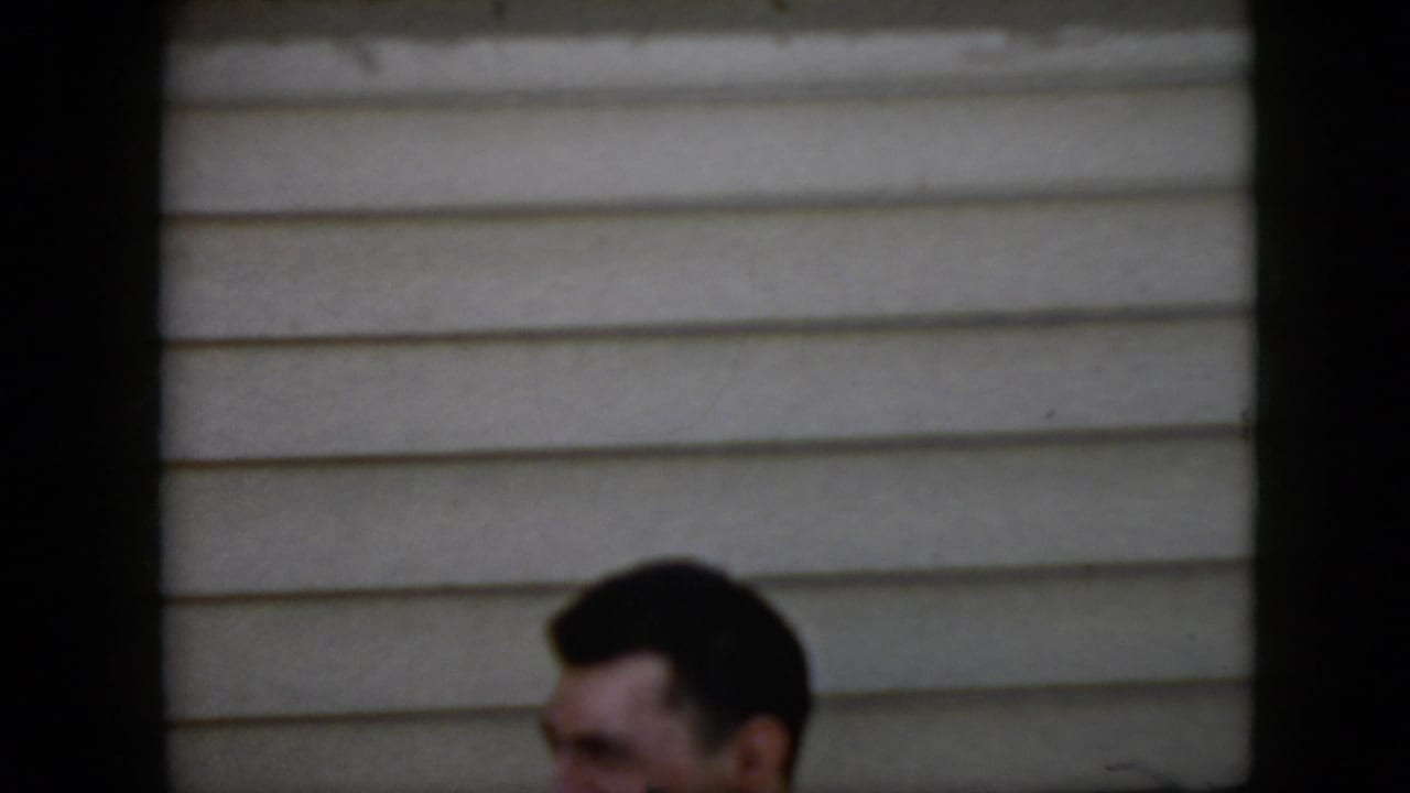 Man's head partly visible behind a low edge against beige horizontal siding.