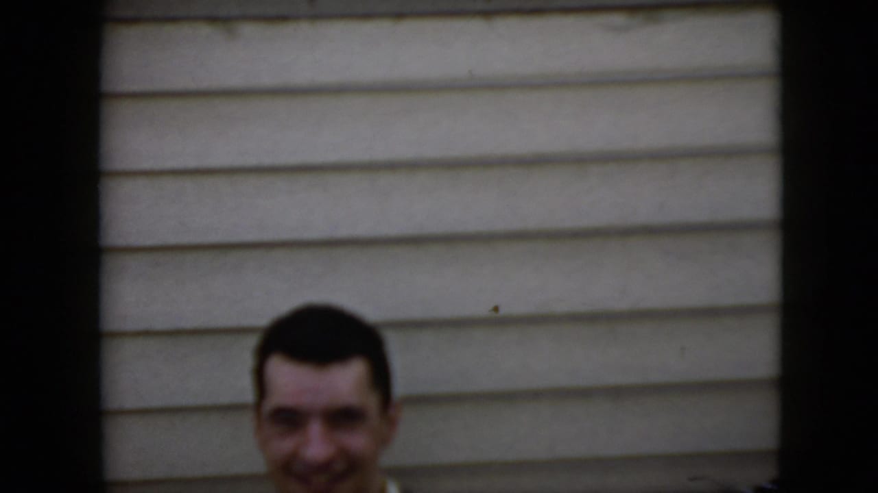 Smiling man partly visible above a low edge in front of beige siding.