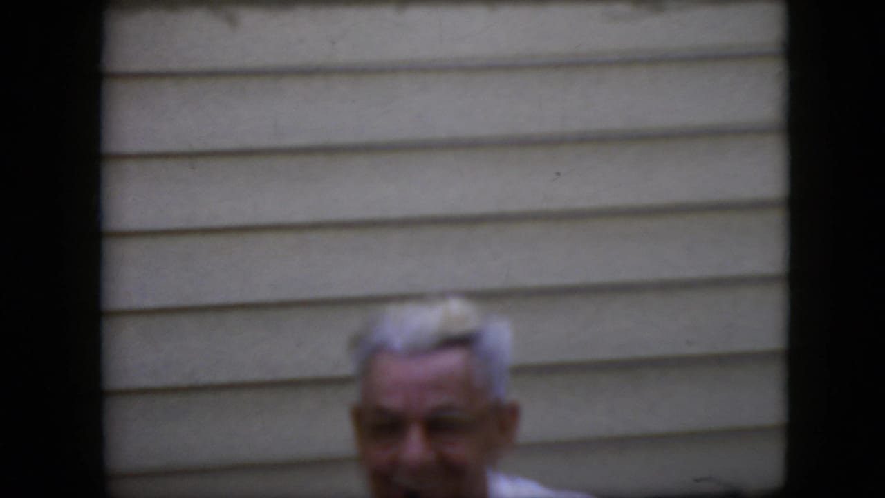 Older man with white hair appears partly cropped against beige siding.