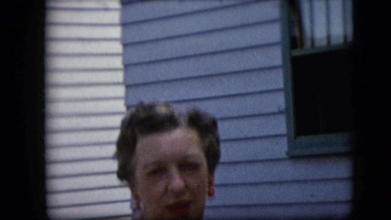 Woman facing the camera beside a green-trimmed window on a light-sided exterior wall.